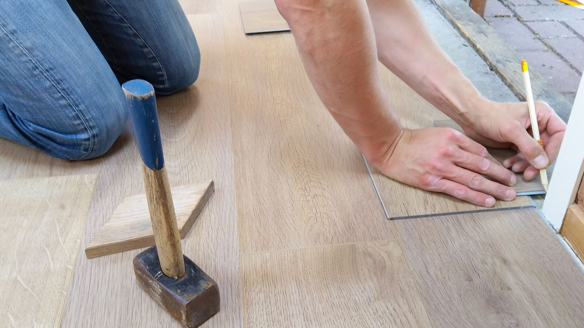 A person laying a tile on the floor with a hammer