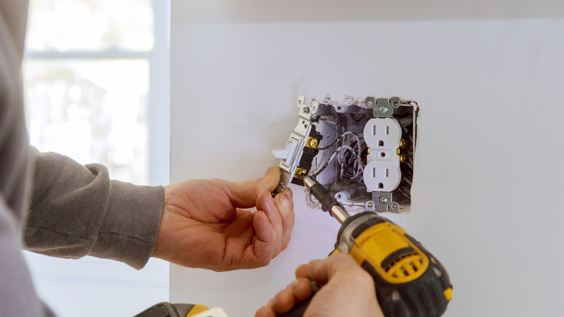 A person using a screwdriver to fix a light switch